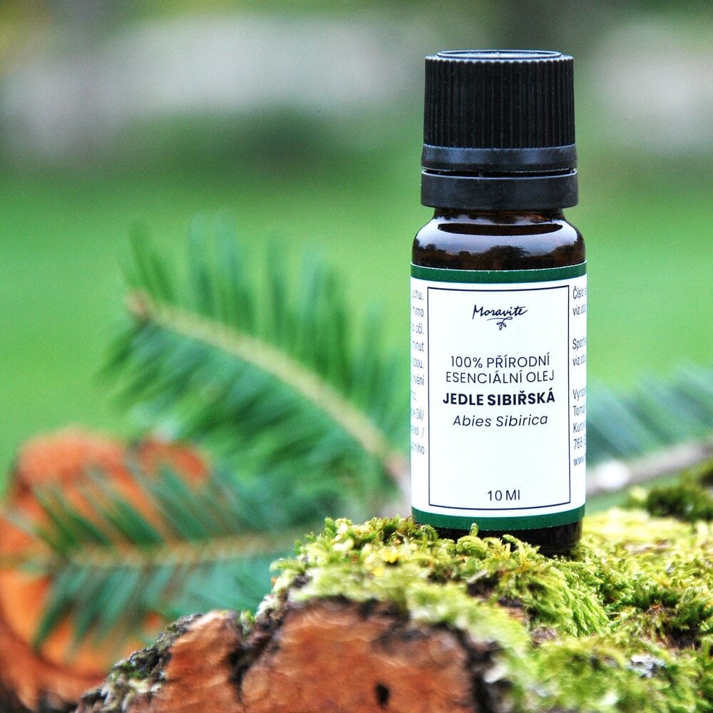 Hnědá skleněná lahvička 10ml 100% přírodního esenciálního oleje Jedle sibiřská (Abies Sibirica) značky Moravité, umístěná na kusu kůry porostlé mechem s rozostřeným zeleným pozadím a větvičkou jehličí.