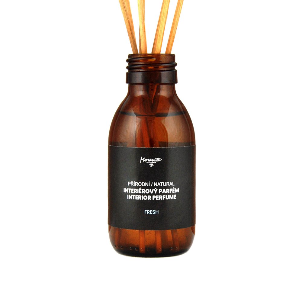 Tmavá skleněná lahvička interiérového parfému s černou etiketou. Na etiketě je bílé logo Moravité a bílé nápisy PŘÍRODNÍ NATURAL INTERIÉROVÝ PARFÉM INTERIOR PERFUME a FRESH. Z hrdla lahvičky vyčnívá pět dřevěných tyčinek. Produkt je na bílém pozadí.