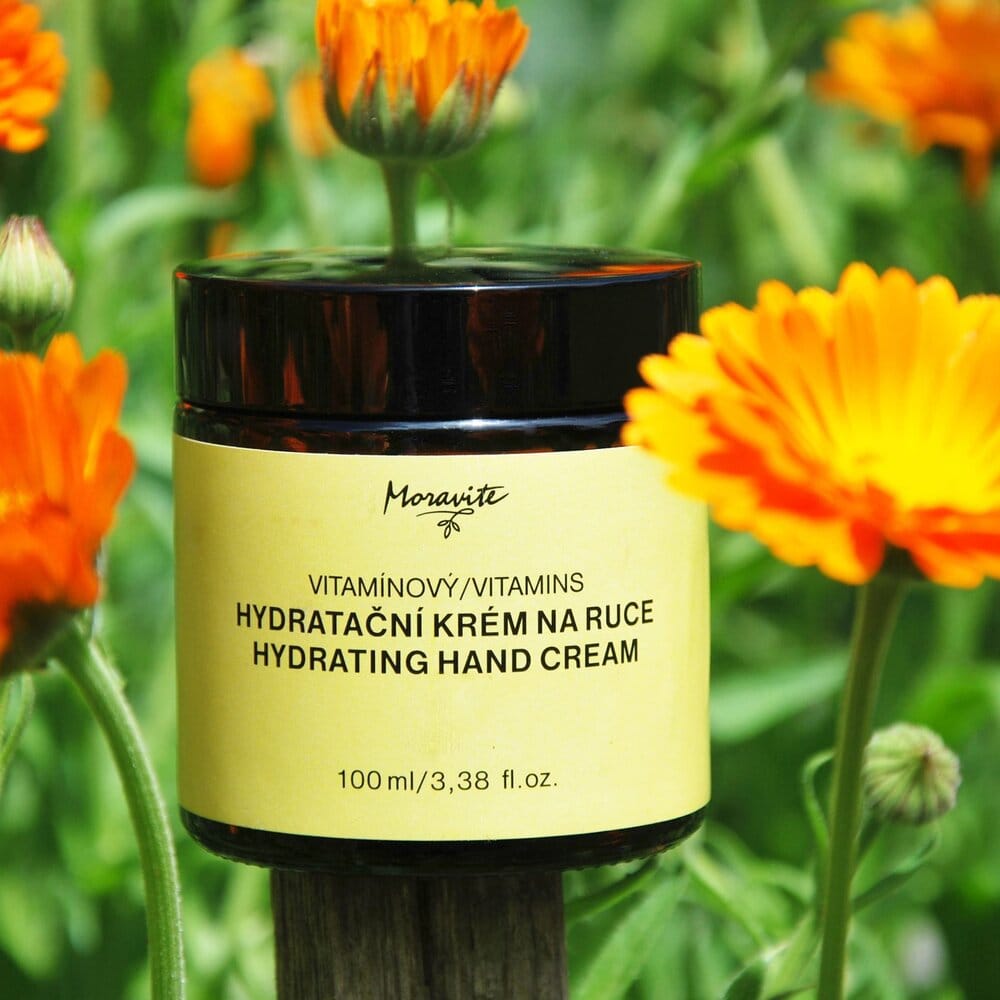 Vitamínový hydratační krém na ruce Moravite (100 ml) se žlutou etiketou na dřevěném kůlu u květu měsíčku lékařského.