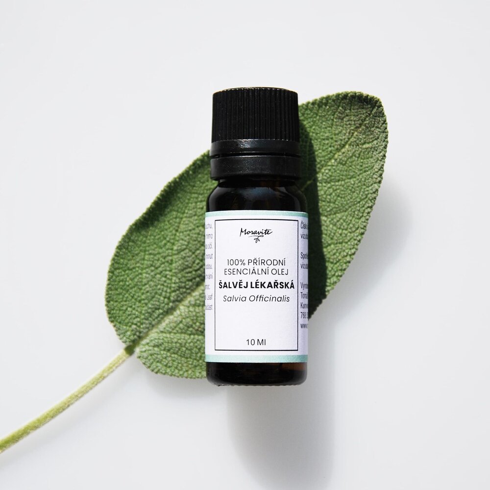 Lahvička 100% přírodního esenciálního oleje Moravité Šalvěje lékařské (Salvia Officinalis) o objemu 10 ml položené na listu šalvěje lékařské s bílým pozadím.