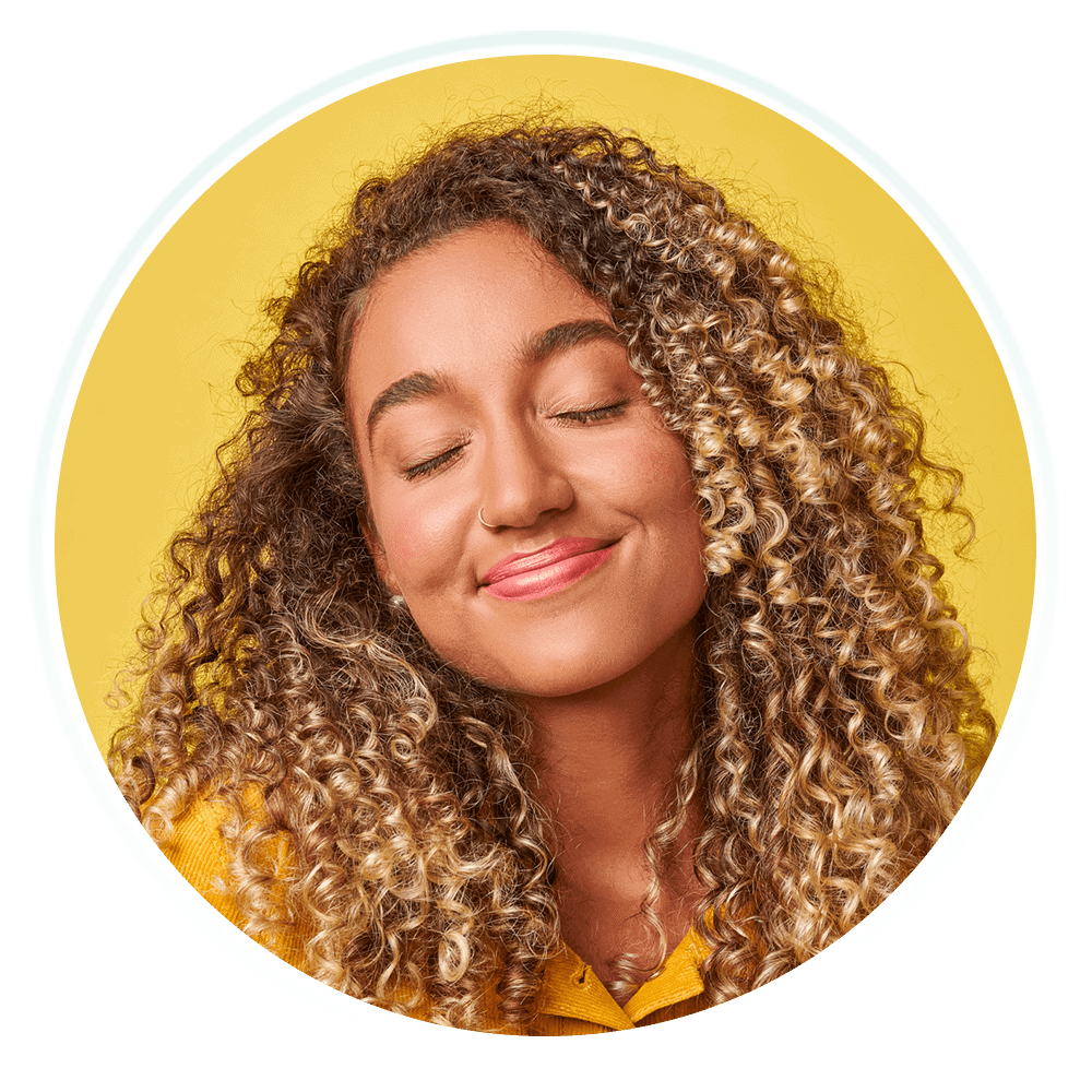 A young woman with curly hair with closed eyes and a big smile.