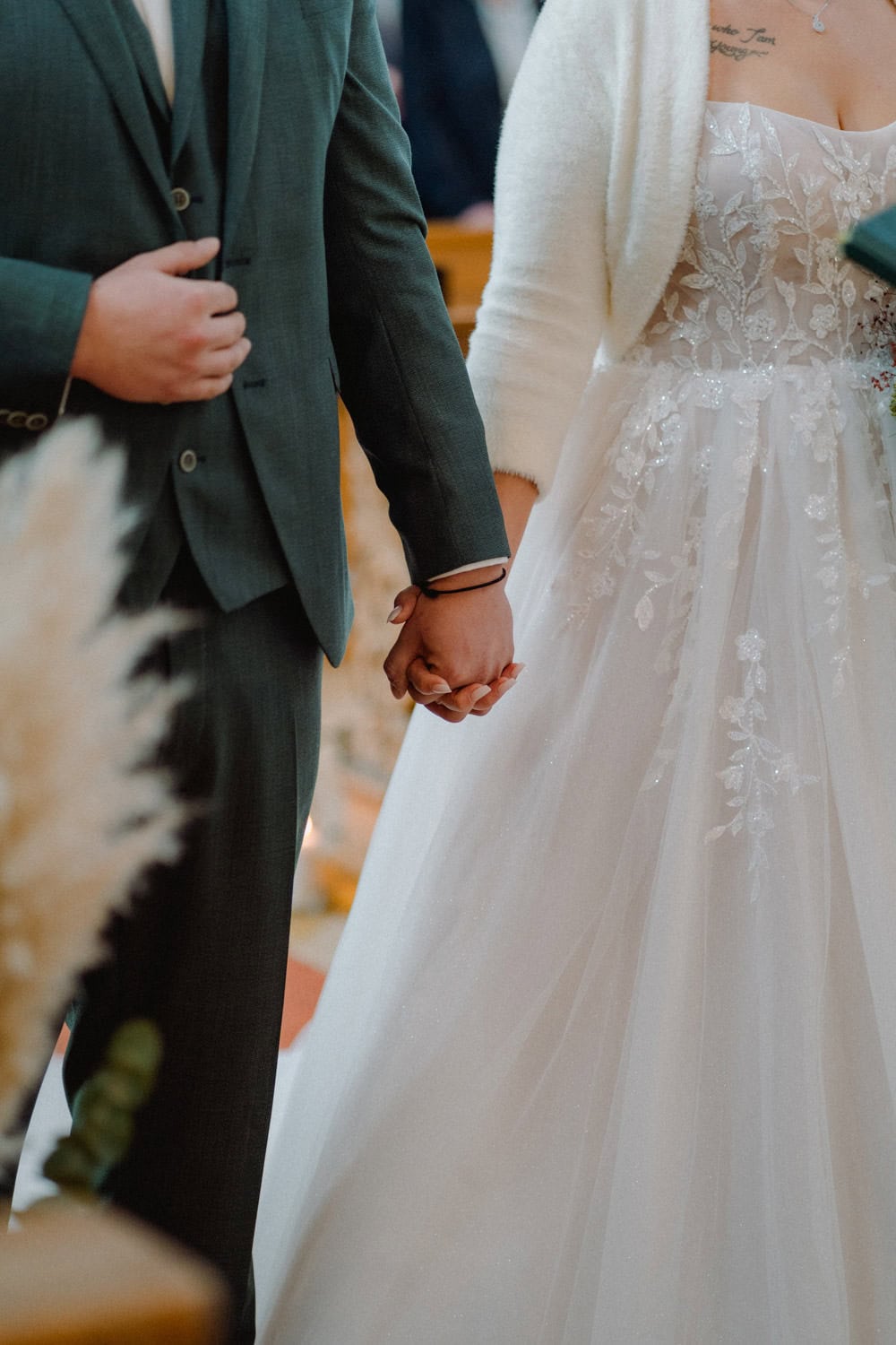 Im warm beleuchteten Ambiente des Hammerschlosses Stodl Schmidmühlen steht ein Paar während der Trauungszeremonie eng beieinander. Die Person links trägt einen dunklen Anzug, die rechte ein weißes Brautkleid mit Spitzendetails, ihre Hände sind zärtlich verschränkt.