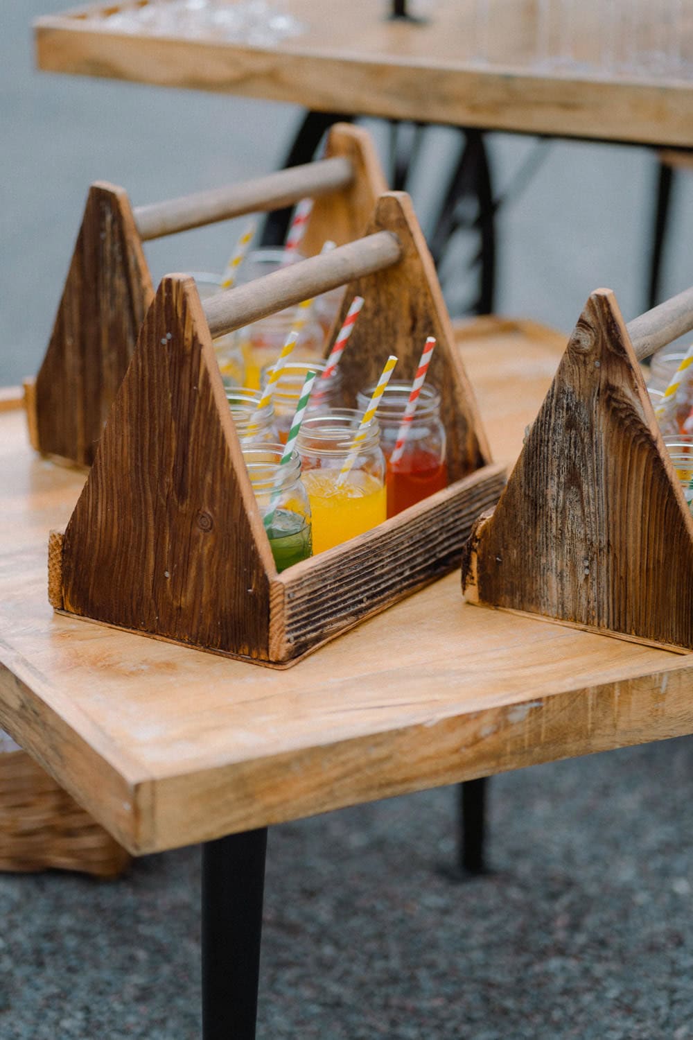Auf einem Tisch stehen Holzträger mit Glasflaschen voller bunter Getränke, die jeweils mit einem gestreiften Strohhalm versehen sind. Im Freien gelegen, lässt dieses charmante Arrangement auf eine zwanglose oder rustikale Veranstaltung im Hammerschloss Stodl in Schmidmühlen schließen.