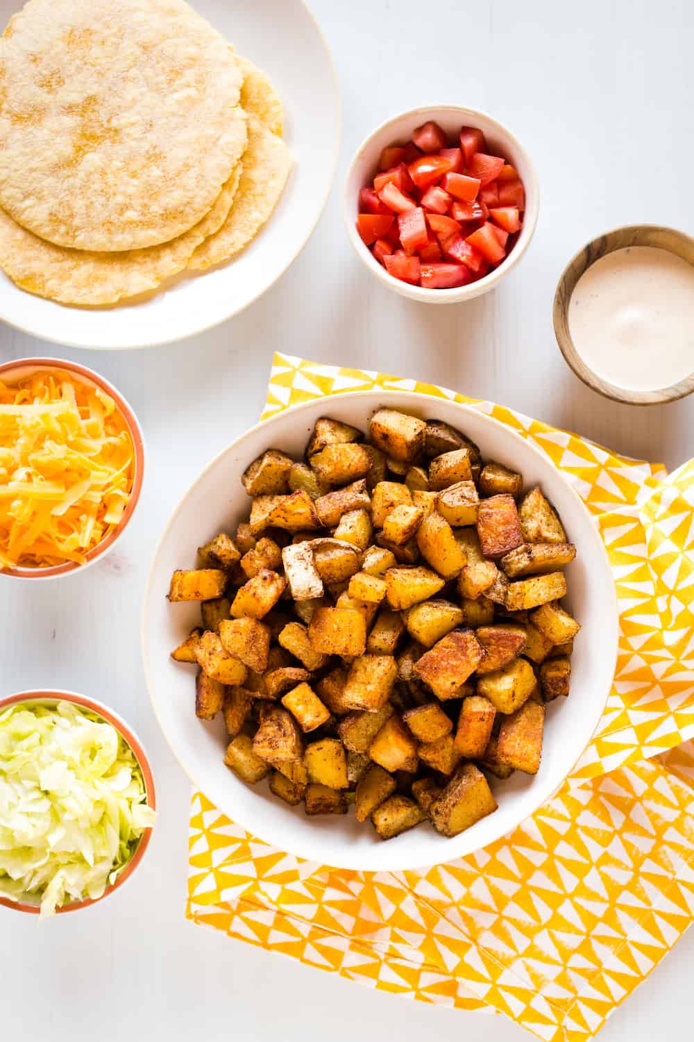 spicy potato taco ingredients - tortillas, cheese, lettuce, tomatoes, potatoes and chipotle sauce