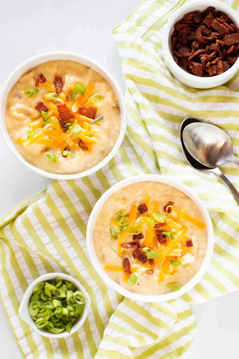 bowls of baked potato soup topped with cheddar, bacon and scallions