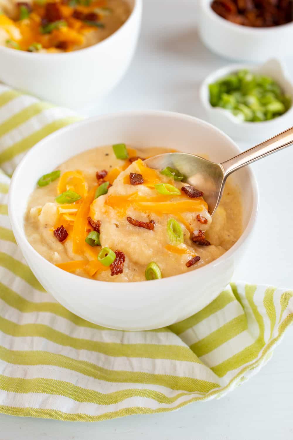 bowl of baked potato soup topped with cheddar, bacon and scallions