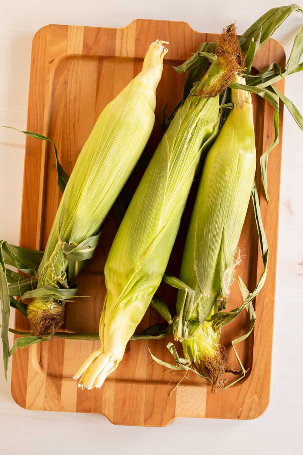 fresh ears of corn on a cutting board