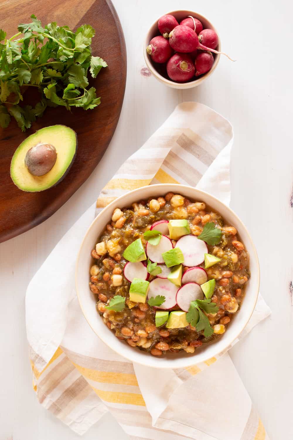 bowl of vegan tomatillo stew with beans, hominy, radishes, and avocado