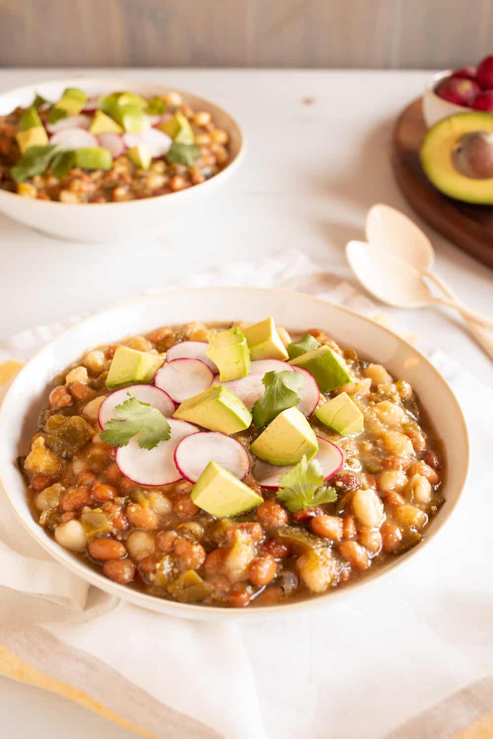 bowls of vegan tomatillo stew with beans, hominy, radishes, and avocado