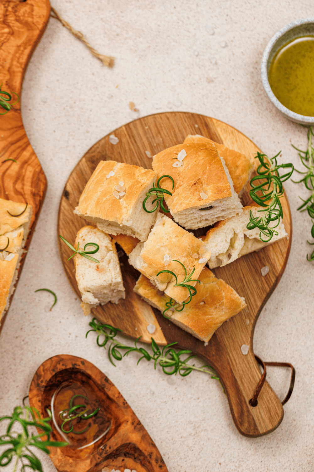 Top-down view of cubed rosemary focaccia bread on a wooden board with a small bowl of olive oil dipping sauce.