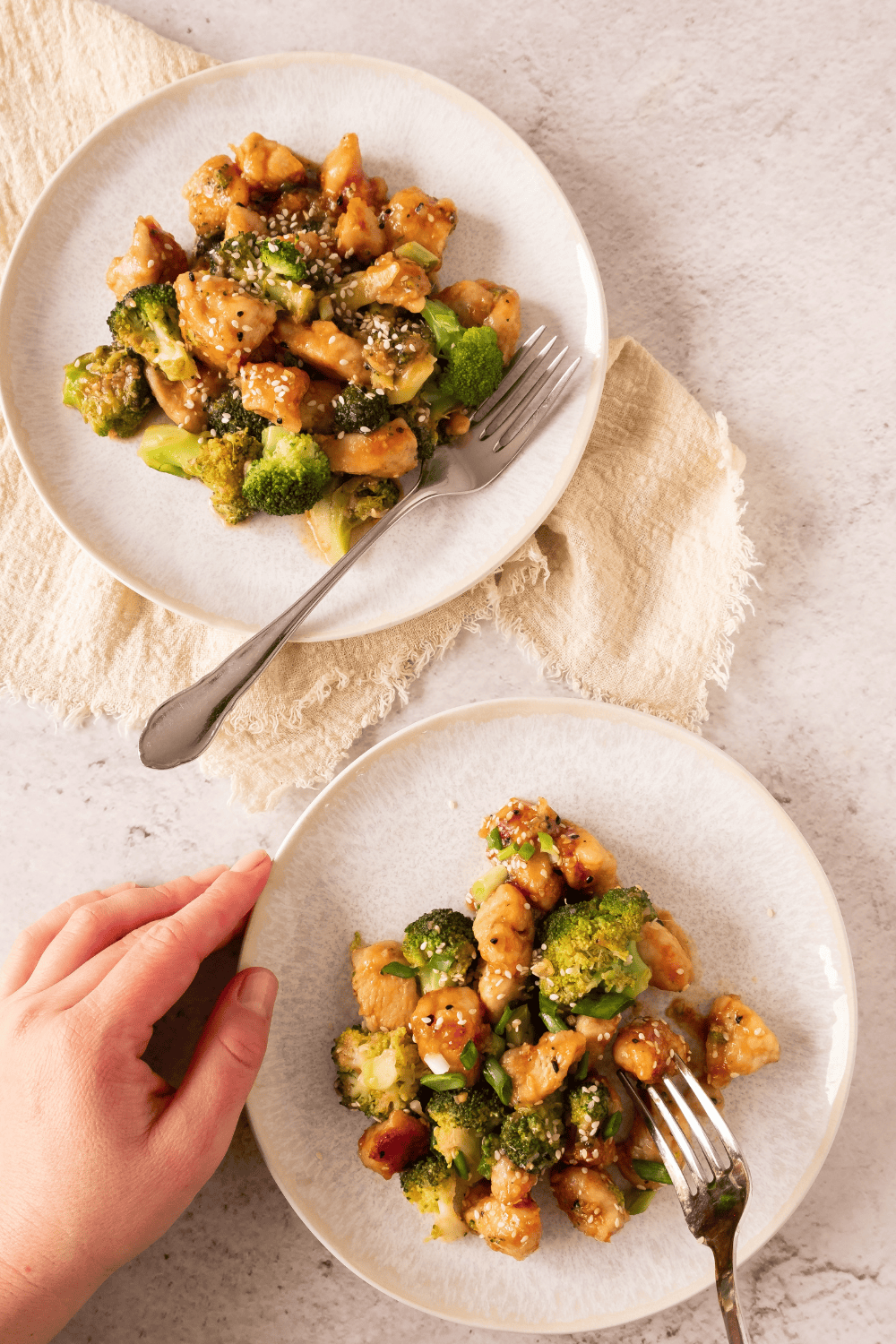 Two plates of homemade honey garlic chicken with a hand holding a fork.