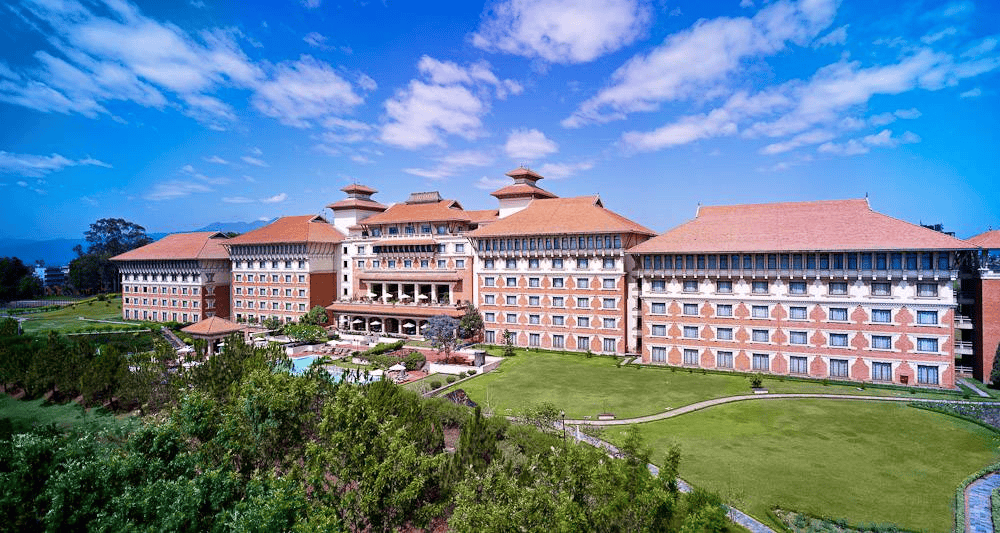 A wide view of the grand Hyatt Regency complex showcasing traditional Nepalese-style brick and tile architecture, sprawling green lawns, and manicured gardens under a blue sky.