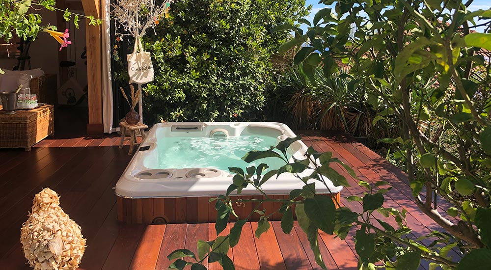 Un spa est encastré dans une terrasse en bois, entourée de verdure.