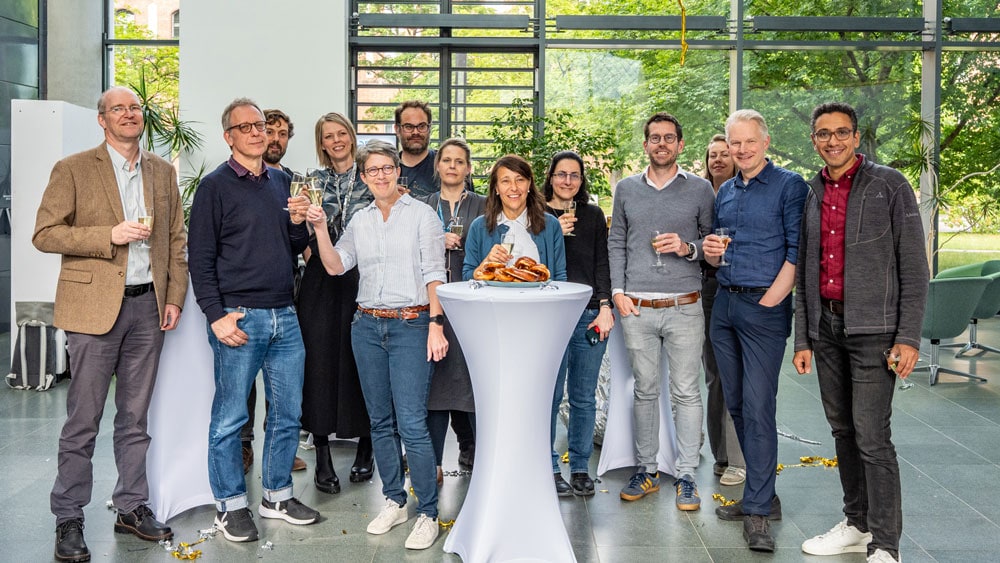 The group photo shows people involved in the ImmunoPreCept Cluster of Excellence. They are celebrating the Cluster's approval.