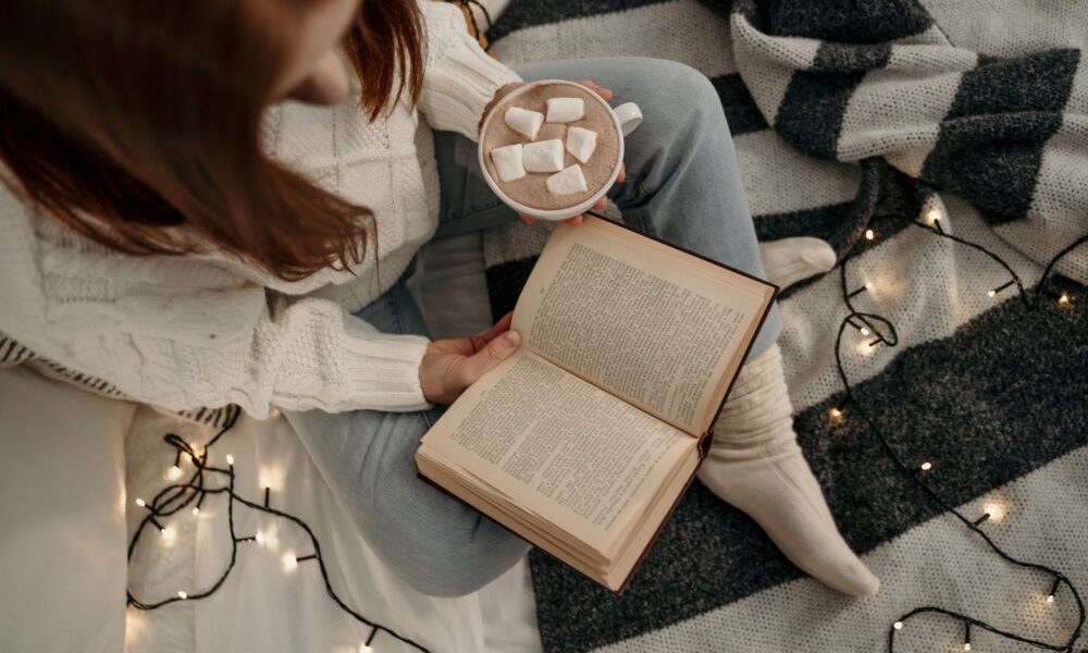 National Hot Chocolate Day: woman holding a book and a cup