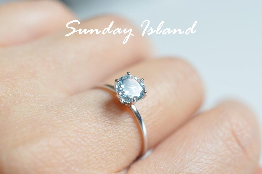 a blue aquamarine stone set in white gold with six prongs on a hand