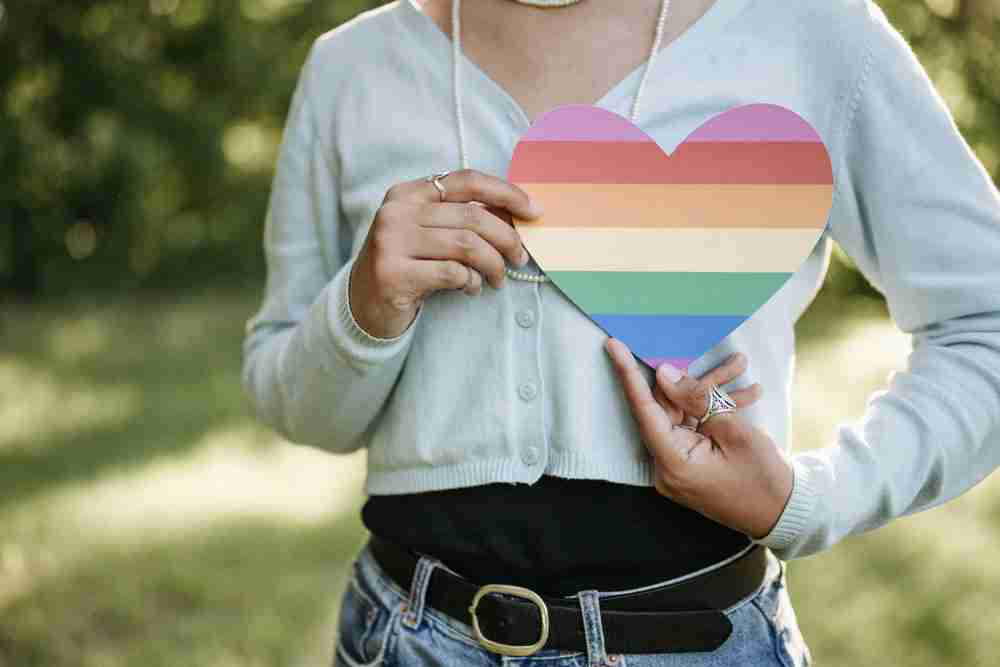 Person outdoors, holding a rainbow heart cutout to show support for Pride and LGBTQ+ equality. Start LGBTQ therapy near me