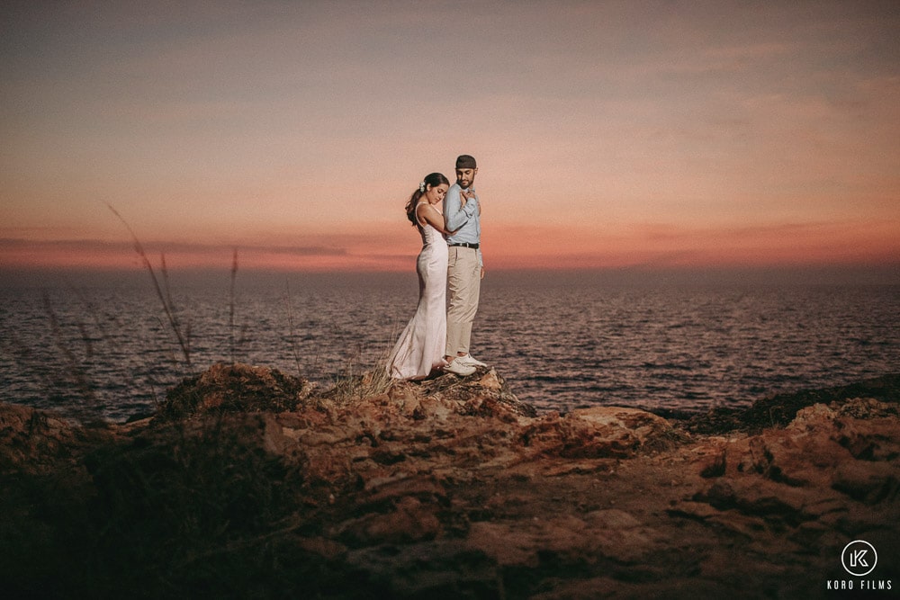 Couple embracing on the rocky Rayong coastline under a pink evening sky