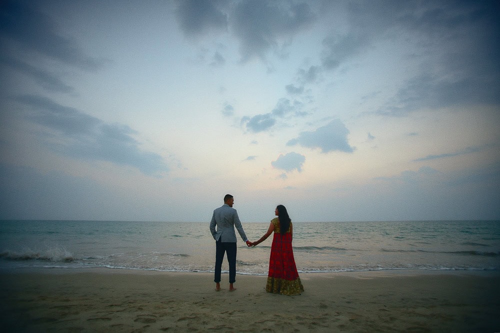 Couple holding hands on a Phang Nga beach beneath an evening sky