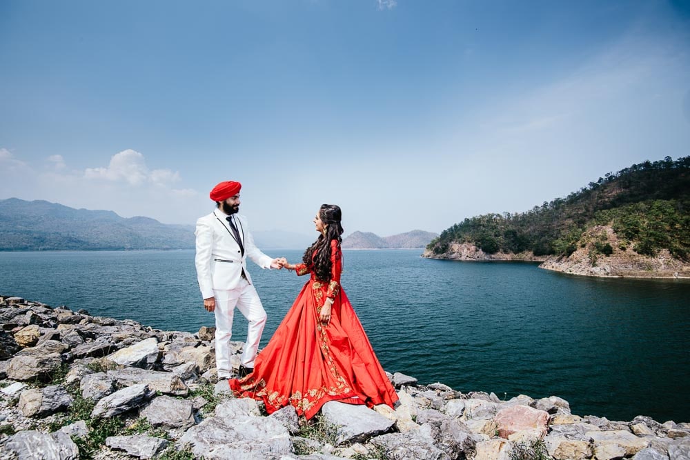 Couple in red and white outfits beside a lake and mountains in Kanchanaburi