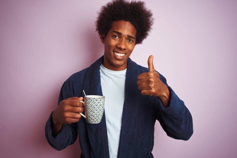 man wearing pajamas holding coffee mug with a thumbs up