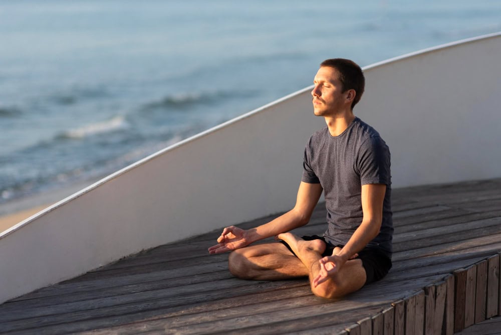 Man practicing meditation in lotus pose near the ocean, embracing mindfulness and calm.