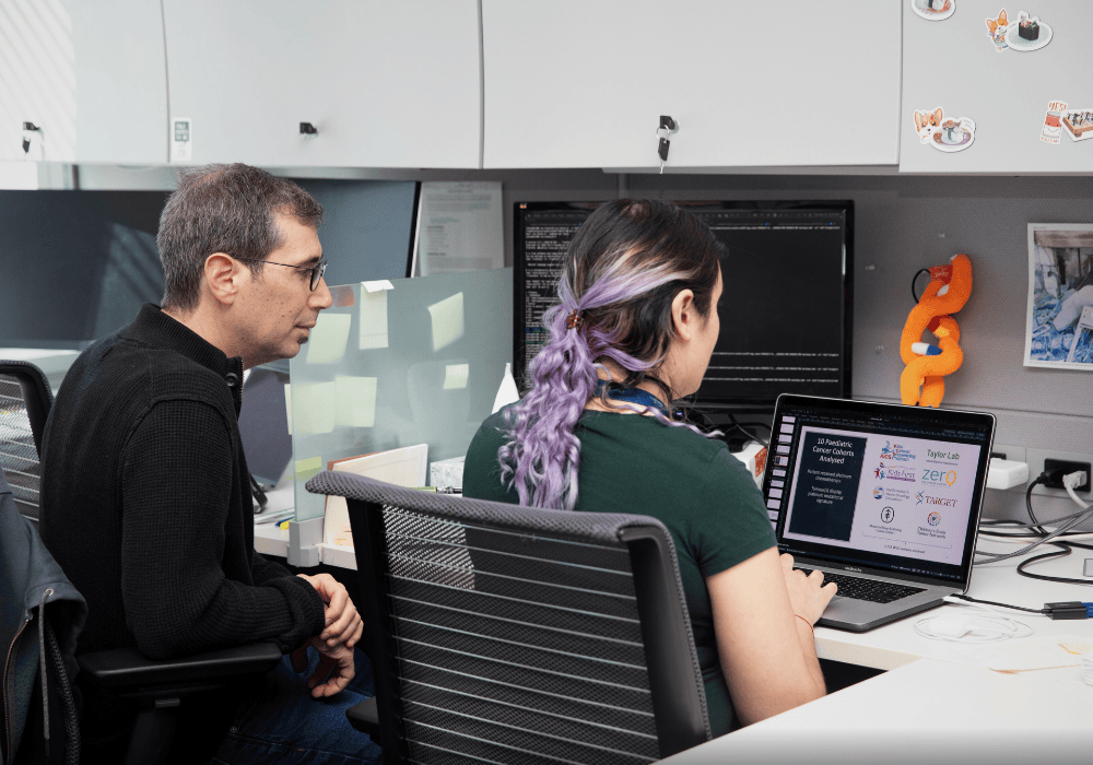 SickKids Researcher Adam Shlien sits beside a colleague in a research office, working on a presentation