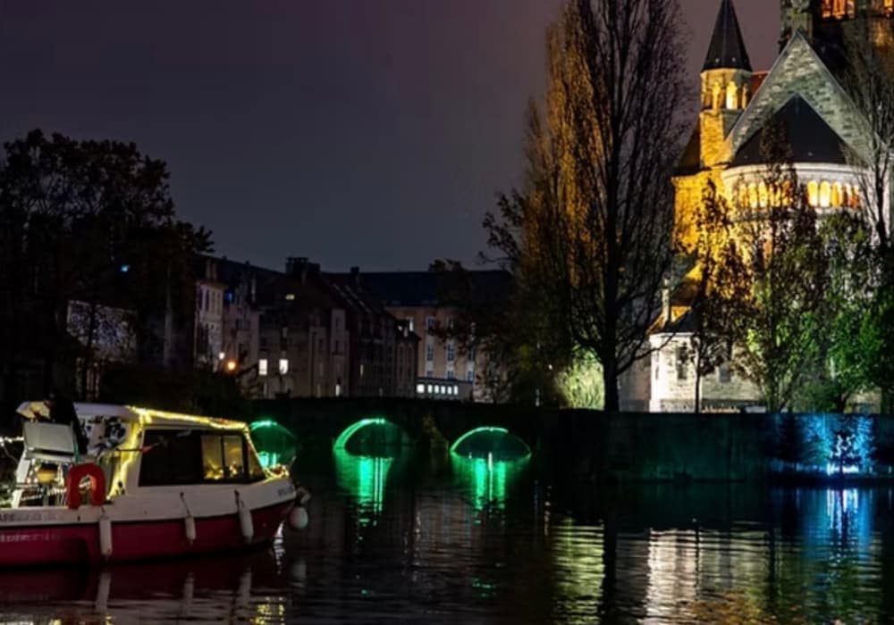 Bateau sur l’eau avec reflets la nuit, temple neuf illuminé en arrière plan 