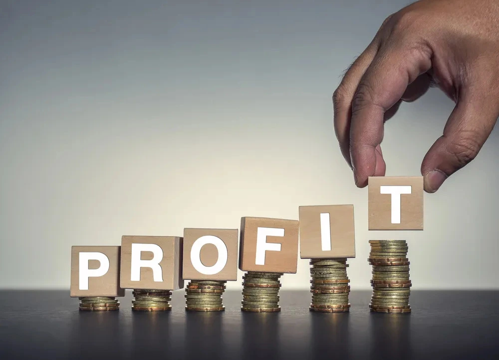 Profit growth concept with hand placing blocks over increasing coin stacks