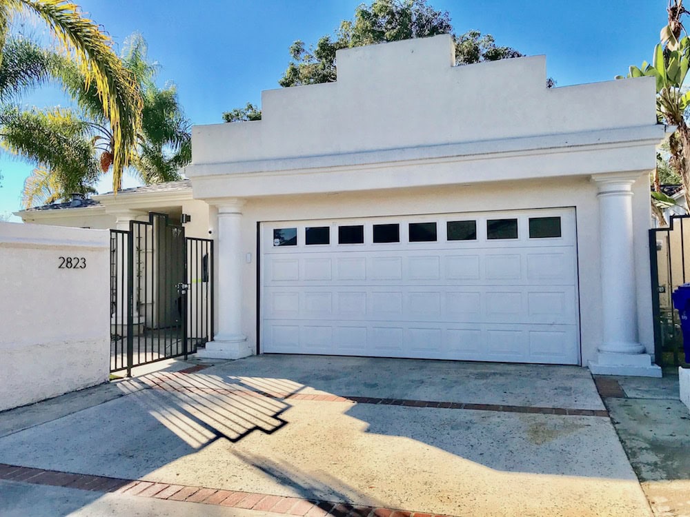 Modern white garage in North Park with Mediterranean-style columns, a stepped parapet roofline, and a gated entryway under bright sunny skies.