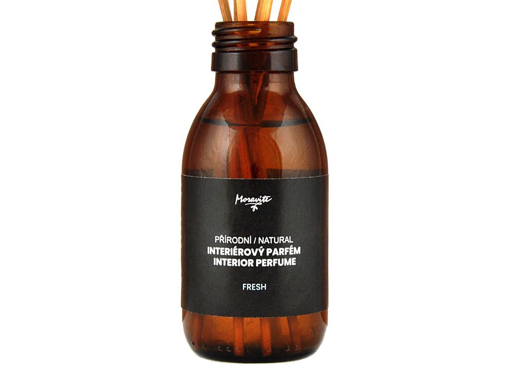 Tmavá skleněná lahvička interiérového parfému s černou etiketou. Na etiketě je bílé logo Moravité a bílé nápisy PŘÍRODNÍ NATURAL INTERIÉROVÝ PARFÉM INTERIOR PERFUME a FRESH. Z hrdla lahvičky vyčnívá pět dřevěných tyčinek. Produkt je na bílém pozadí.