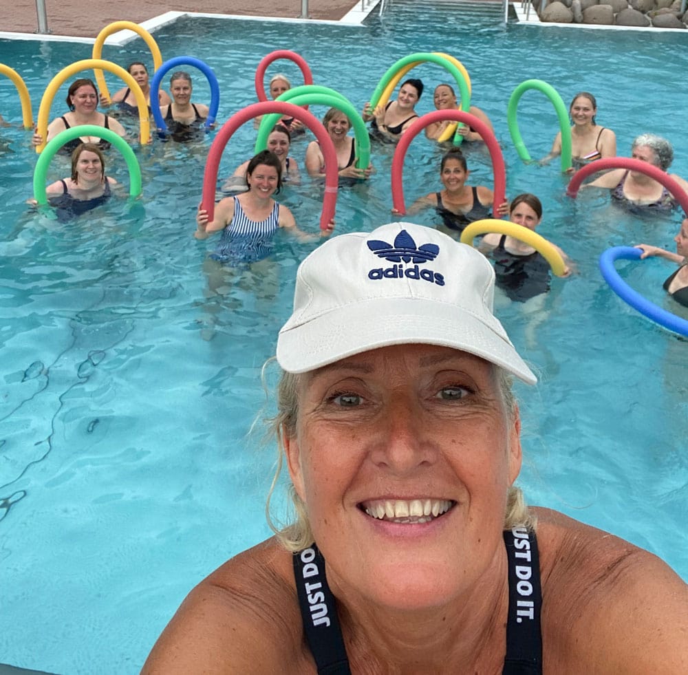 Delphine ist im Vordergrund zu sehen. Im Hintergrund die Teilnehmer im Wasser mit Schwimmnudel.