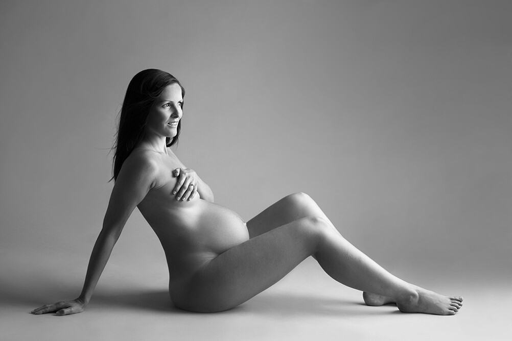 Elegante gravidfotografibilde av gravid kvinne som poserer uten klær, fremhever skjønnheten i svangerskapet i svart-hvitt. Perfekt for gravidefotografi, gravidfoto, svangerskapsfoto, og portrettfotografi for gravide.