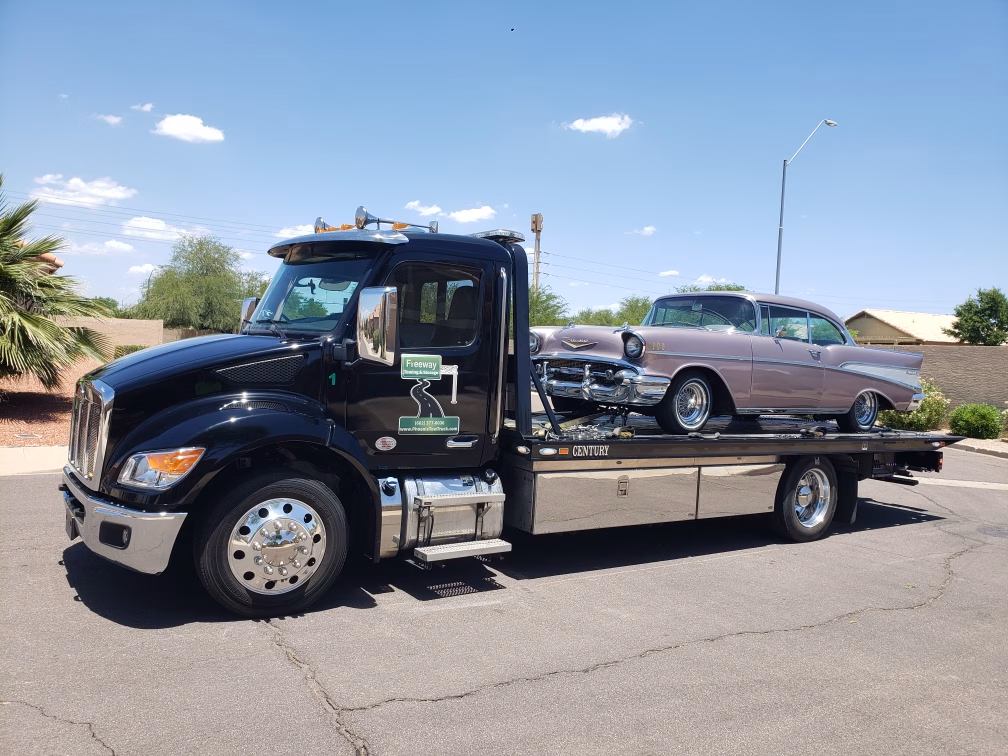 Freeway Towing & Storage black Century flatbed truck transporting a restored 1957 Chevy Bel Air in Phoenix, Arizona on a sunny day