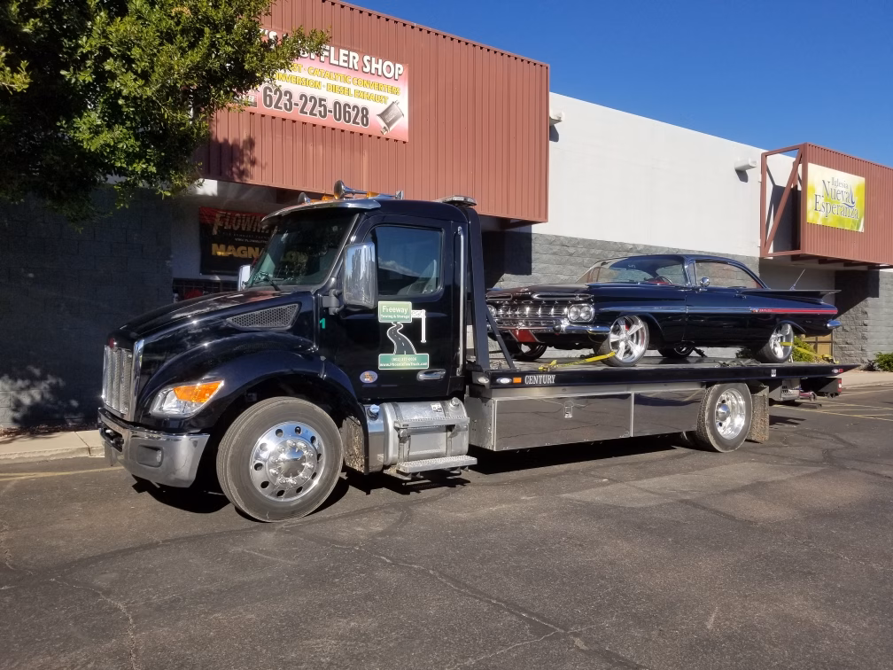 Freeway Towing & Storage black flatbed tow truck hauling a black 1960 Chevy Impala Sport Coupe with custom wheels in Phoenix, AZ