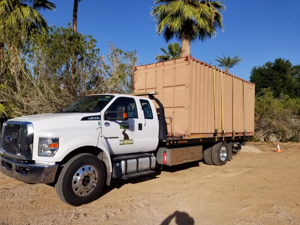 Freeway Towing & Storage flatbed truck transporting a 20-foot storage container through a job site in Phoenix, AZ