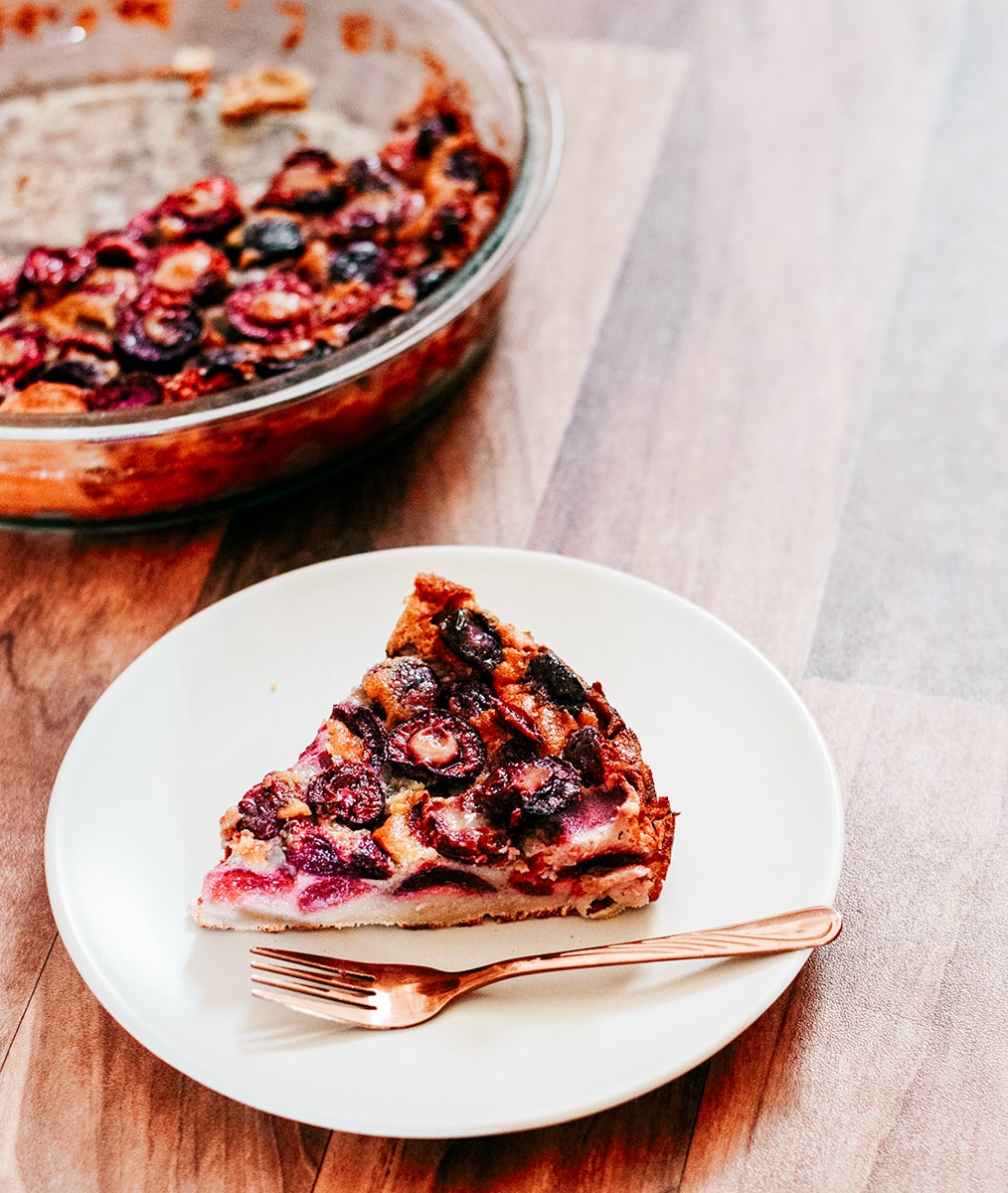 cherry clafoutis on a white plate. More clafoutis on the back