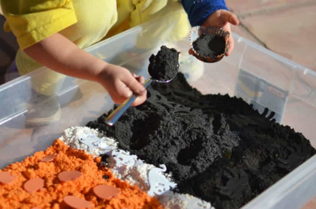 Toddler playing with Halloween orange and black cloud dough sensory bin