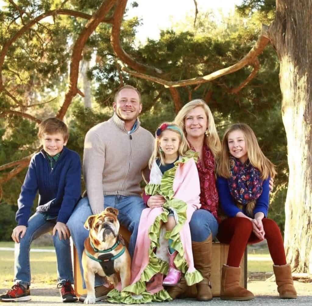 Happy family with dog sitting on park bench under large tree.