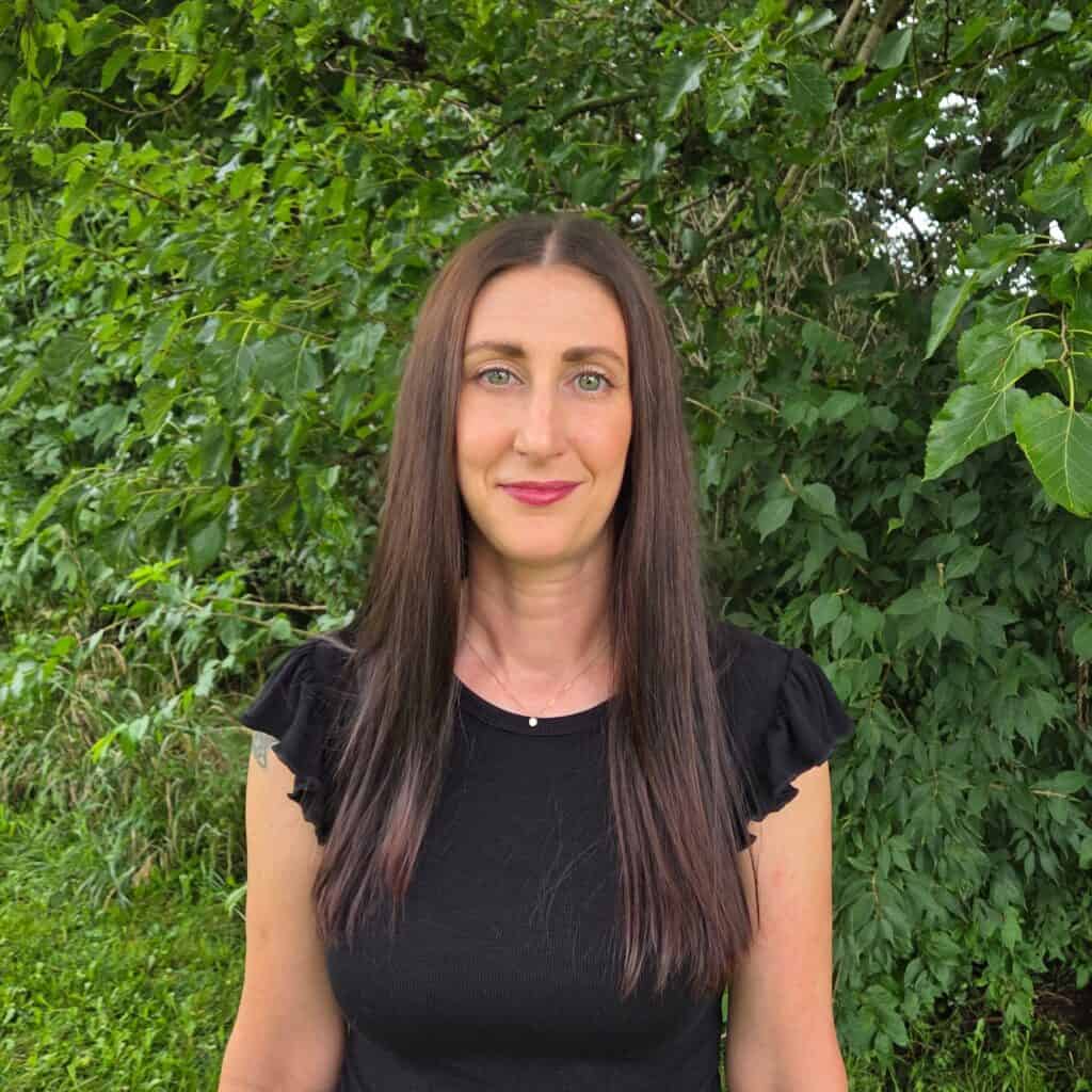 Julie Stewart outdoors with lush green foliage background for vacation planning.