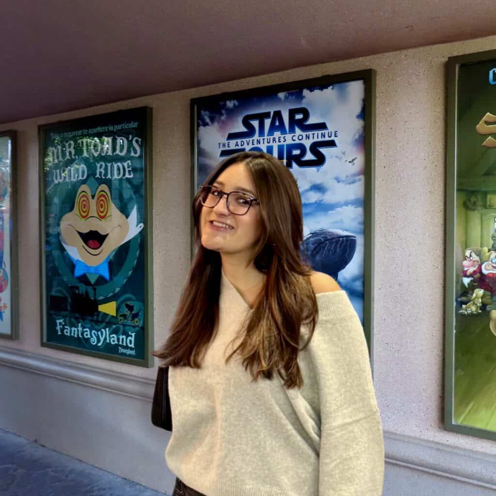 Young woman with glasses smiling at Disney theme park posters.