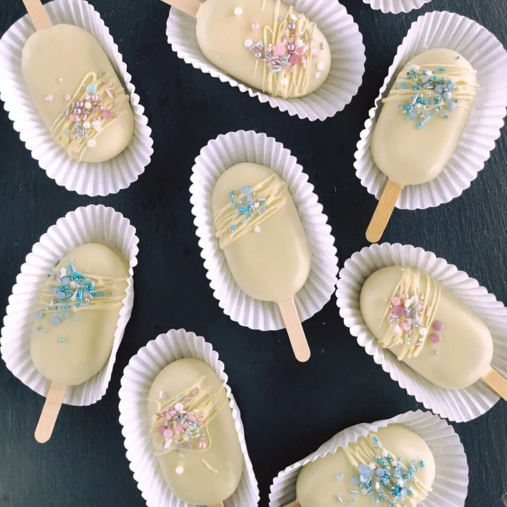 Cakesicles brownie z fruzelina wisniowa w białej czekoladzie dekorowane posypka cukrowa