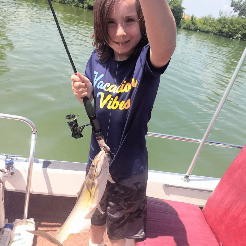 Image illustrates an image of a kid holding a fish on a boat for lake fishing with kids.
