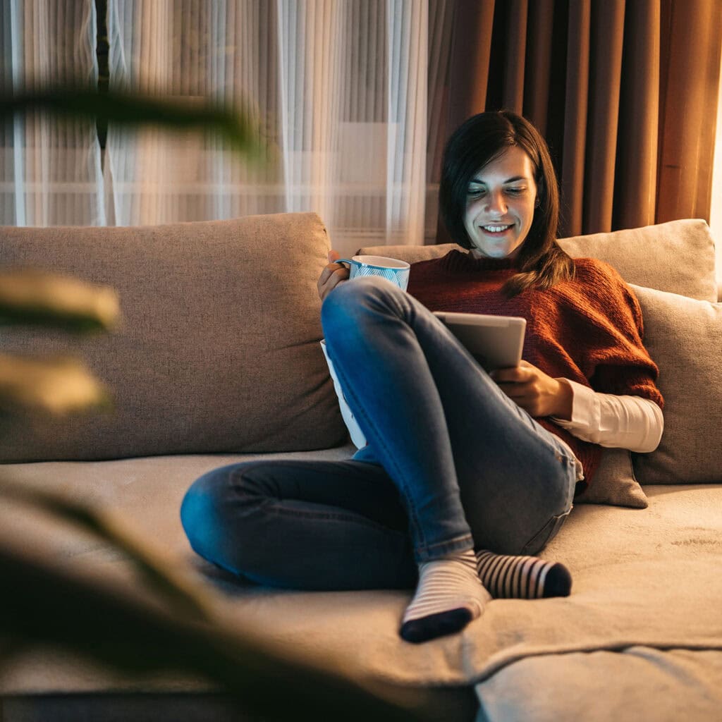Bild på en kvinna som sitter i en soffa och surfar på internet.