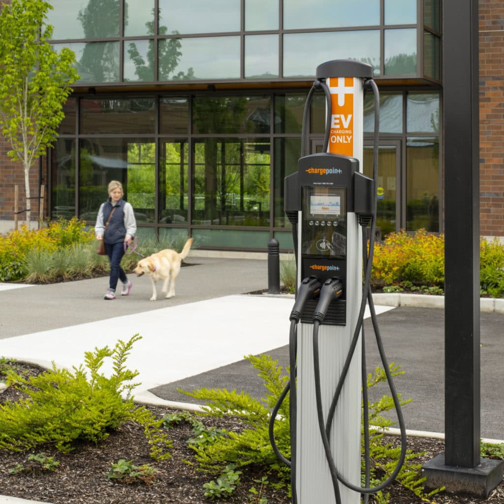 EV charging station in front of a building with a person walking a dog nearby