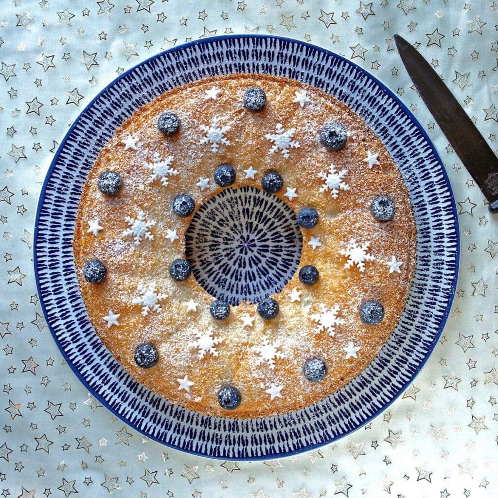 gluten free angel food cake topped with blueberries and sprinkles on a blue plate in the Winter Warming Oven Bakes Cookblogshare