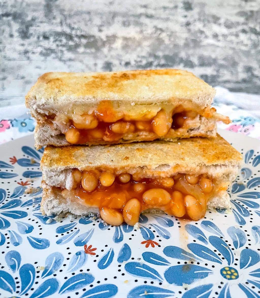 two halves of cheese toastie with beans stacked on plate.