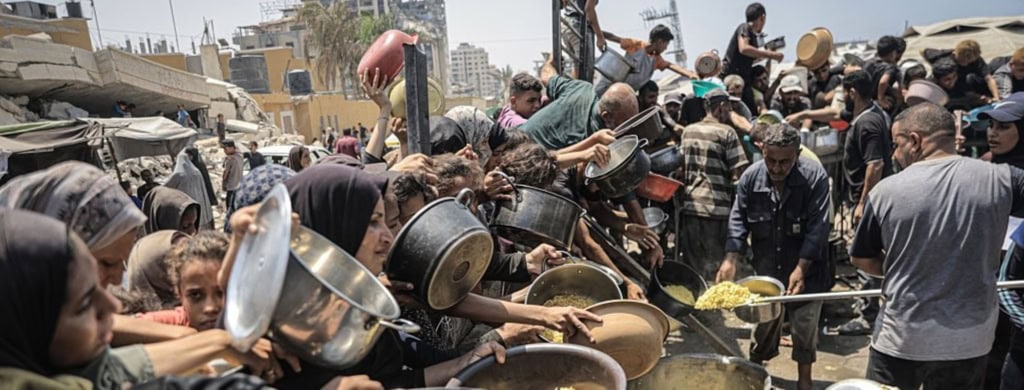 Palestinians wait with pots in their hands as a charitable organization distributes food to Palestinians suffering food crisis under Israeli blockade in Gaza City, Gaza on August 14, 2025. Photo by Ahmed Jihad Ibrahim Al-arini/Anadolu via Getty Images.