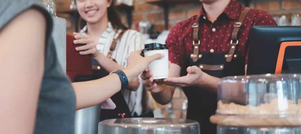 Barista handing a customer a coffee at a cafe counter. Focus on customer's hand receiving the coffee.