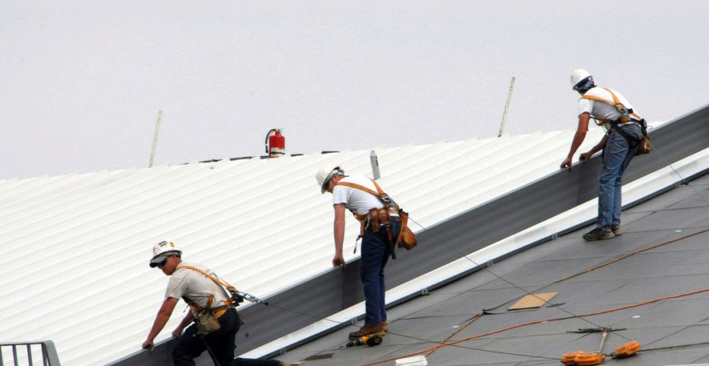 Three roofing contactors carrying a white sheet metal roofing piece.